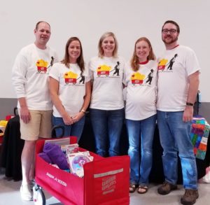 Group of volunteers smiling with a Warrior Wagon filled with supplies